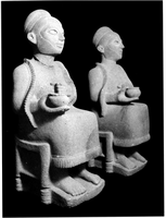 Two seated statues, each depicting a person with a long robe carrying a bowl.