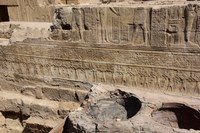 Photo of a portion of a damaged section of wall relief showing several bands of text and iconography, including divine and human figures.