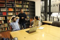 A group of three people gathered around a table and laptop in library in front of bookshelves