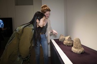 Two students carefully observing ancient stone objects in a gallery display