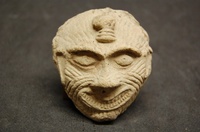 Clay mask depicting human face with wide grin and covered with unusual lines