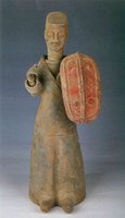 Photo of a ceramic figurine of a robed person carrying a red shield.