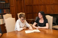 Two students seated at table looking at book in wood-panelled classroom