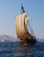 Photo of a sailboat on the water with a fortified building and hills in the background