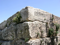 Corner of an ancient building made of stone blocks with inscribed text on the highest block.