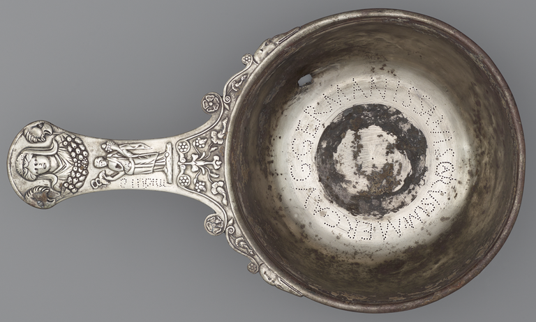 Photograph of a bowl from above with a Latin inscription inside the cup and, on the long handle, a female bust flanked by two bird heads and a female figure holding caduceus and cornucopia