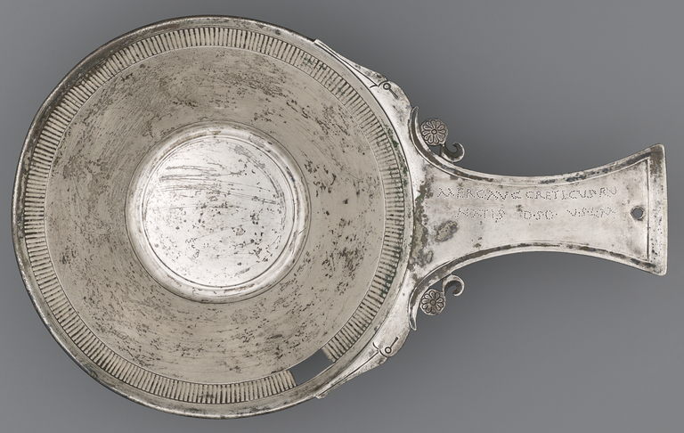 Photograph of a silver bowl from above. On the handle there is an incised Latin inscription.