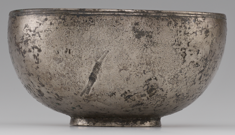 Photograph from the side of a hemispherical silver bowl with a short circular base and thin, banded rim. No figurative decoration is visible.