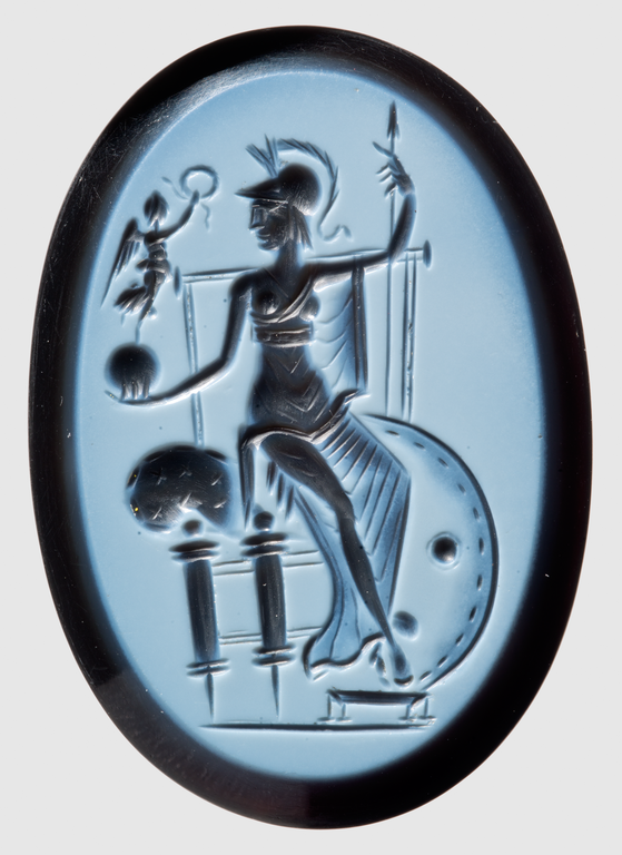 Photograph of engraved gem depicting a female figure seated on a throne with a plumed helmet on her head. In one hand she holds a spear vertically, in the other she supports a sphere atop which stands a winged victory holding out a wreath toward the main figure's head. At the foot of the throne is a scroll, a shield, and a footstool.