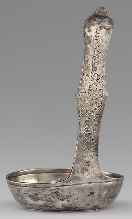 Photograph of a silver ladle with the back of the handle oriented toward the viewer. The Latin inscription is clearly visible.