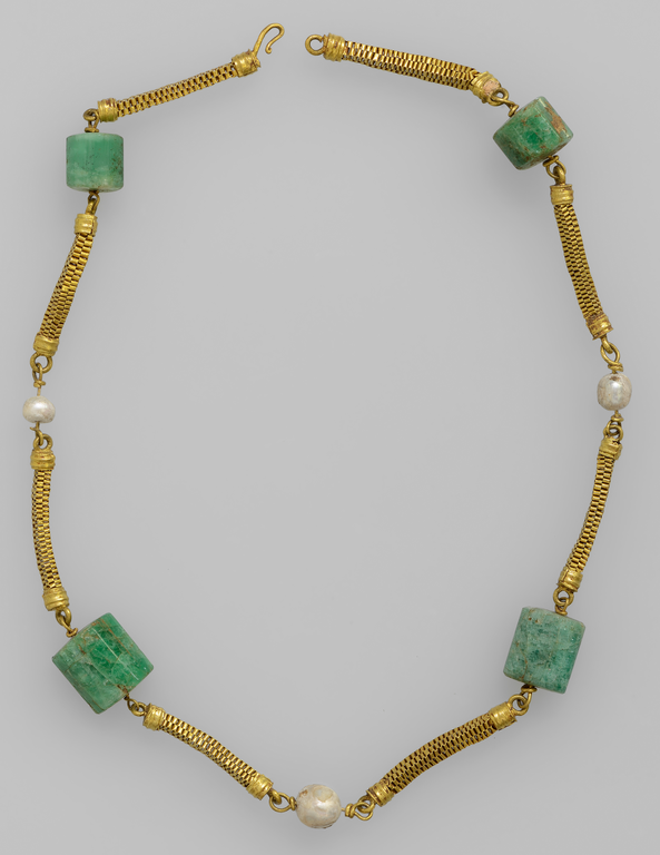 Photograph of a necklace made of alternating pearls and cylindrical emeralds, connected by lengths of braided gold chain.
