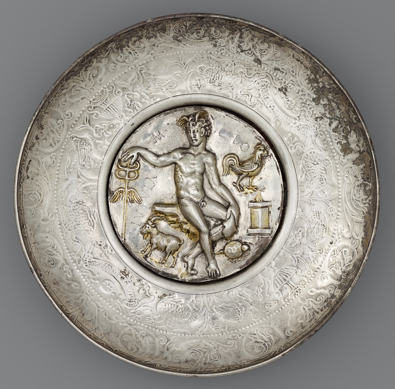 Photograph of a silver bowl with a large central medallion depicting a nude, seated Mercury with caduceus and wings on his head. An altar, a rooster, a ram, and a tortoise are also depicted.