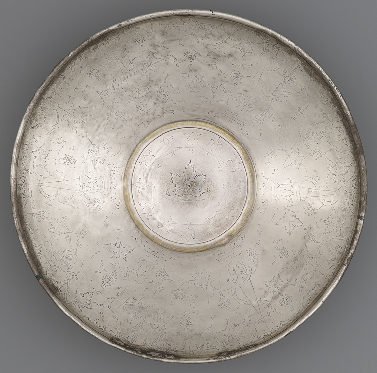 Photograph of a silver plate with gold trim, decorated with an incised pattern of grape vines and birds