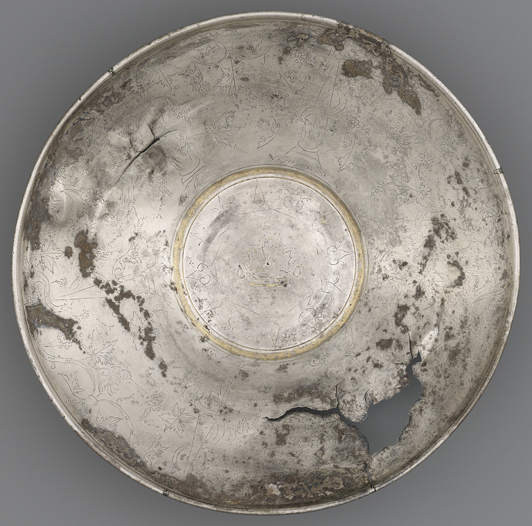 Photograph of a silver plate with gold trim, decorated with an incised pattern of grape vines and birds