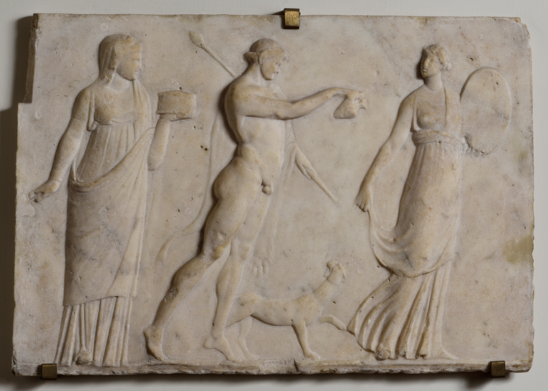 Photograph of a marble relief depicting a female figure holding a large, oval object, a nude male figure holding a thyrsus and pouring something a jar, a panther looking up at the male figure, and a second female figure holding a round, lidded container.