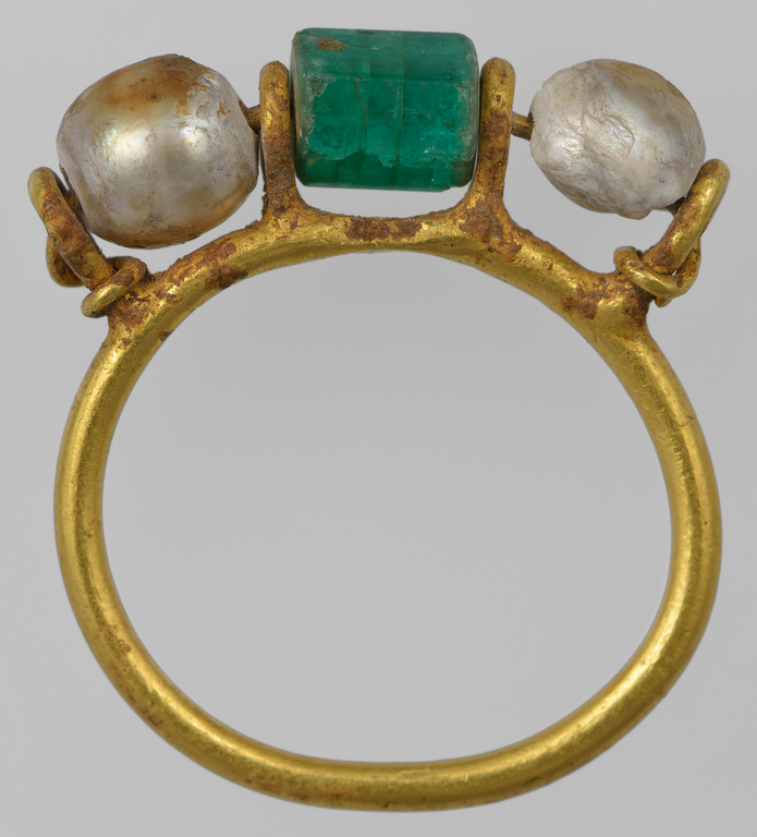 Photograph of a gold ring bearing a cylindrical emerald and two pearls.