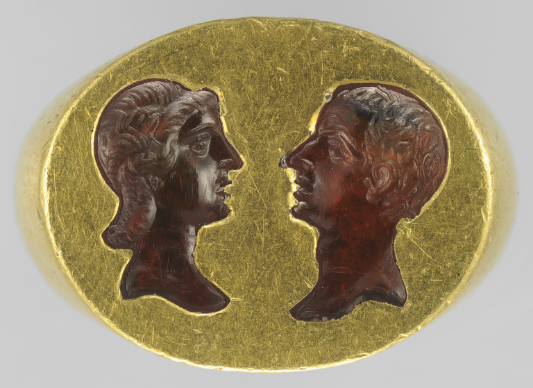 Photograph showing the bezel of a gold ring into which has been set two carnelian busts, one male and one female, facing each other.