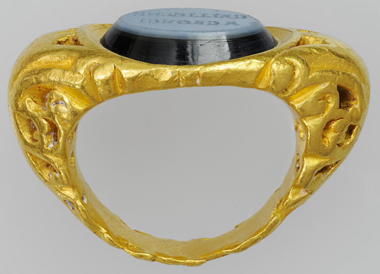 Photograph of a gold ring with a round, flat-topped nicolo (onyx) stone. The flat surface of the stone carries a Latin inscription.