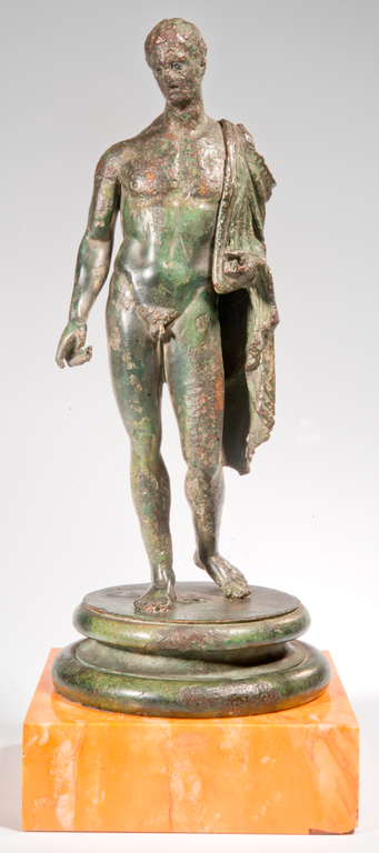 Photograph of a bronze statuette depicting a nude male figure standing contraposto. A cloak is thrown over his left shoulder and his right arm extends down and forward.