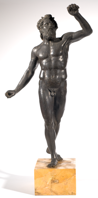 Photograph of a bronze statuette depicting a nude, bearded male figure with small horns on his head. He is stepping forward, with one arm bent and raised above his head and the other extended down and to the side.