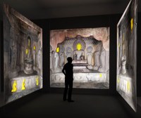 Photograph of a virtual space projected on three walls of a dark room: a cave containing sculptures seems to be depicted.