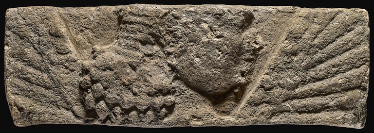 Rectangular brown brick with a molded, raised-relief face representing a female figure in profile (facing right) with wings flanking her side. The figure is shown from the neck up, but her forehead is absent.