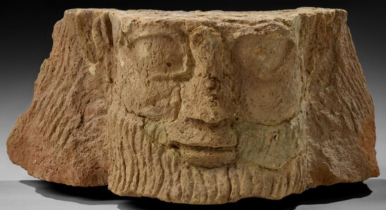 Clay structure representing the front of a man's face, but cropped so that his forehead and chin are absent. His skin, beard, and hair are unpainted brown clay.