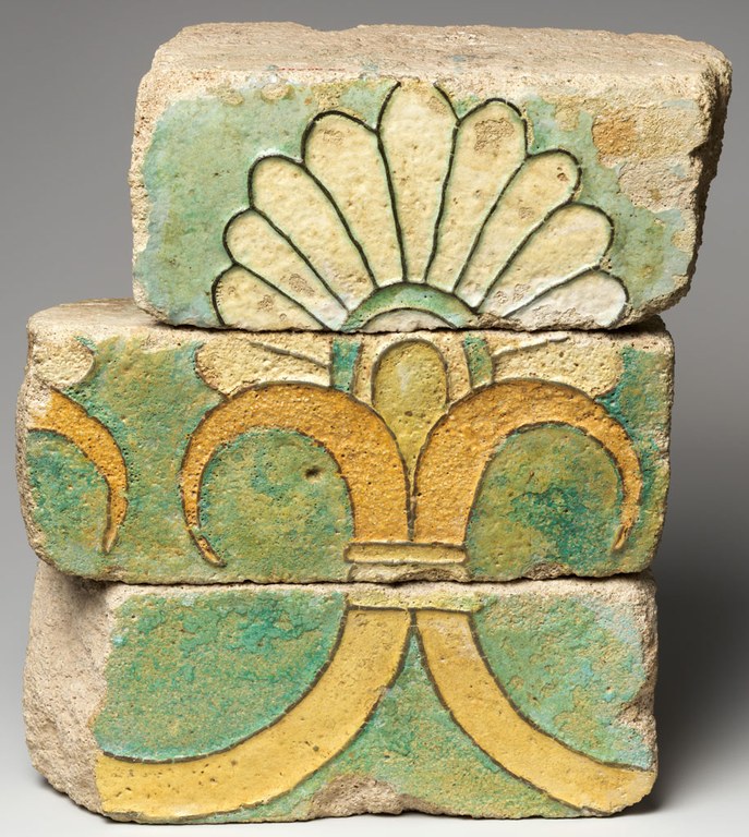 Three fragmentary bricks stacked one on top of the other to form a single image of a stylized palmette. The bottom brick shows the bottom of the plant, the middle brick the center stem, and the top brick the blossom. The bricks are glazed in a siliceous material in bright green, off white, and yellow hues.