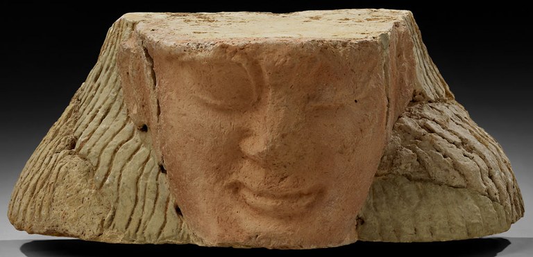 Clay structure representing the front of a woman's face, but cropped so that her forehead and chin are absent. Her skin is unpainted brown clay while her hair is painted yellow.