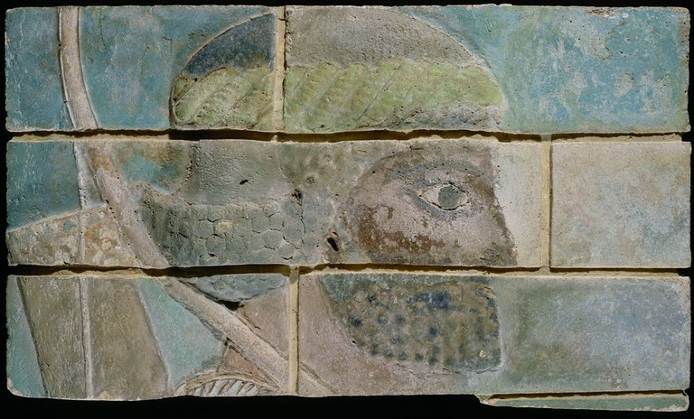 Panel of molded and glazed bricks forming the image of the head of an archer in profile. Part of his bow and arrow are also visible. The colors on these bricks are bluish-green, olive green and light brown.
