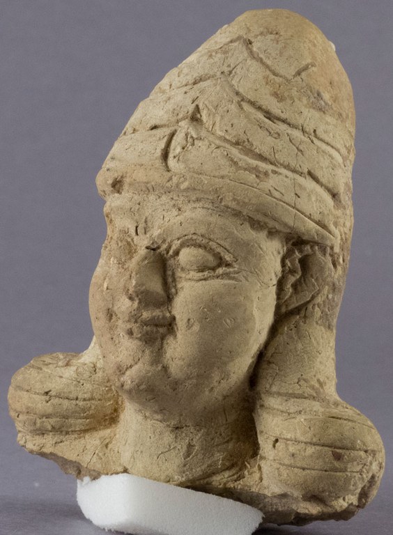 Hand modelled clay figurine of a deity head with a hair dress.