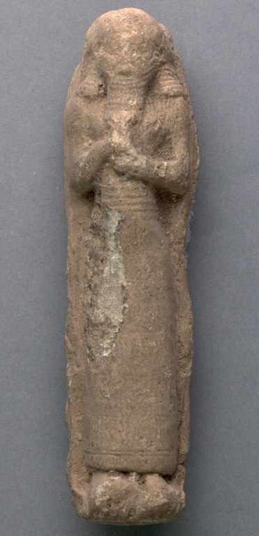 Molded clay figure of a man or a priest holding a vase. The man is wearing a lengthy dress and has a long beard.