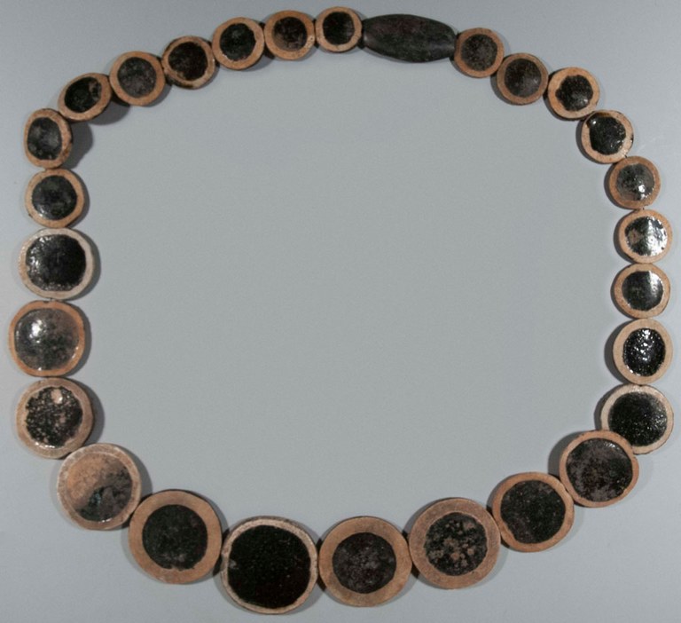 A reconstructed necklace of eyestones. The necklace is made out of glazed vitreous material and stone. Each eyestone is black with a golden yellow concentric circle around it.