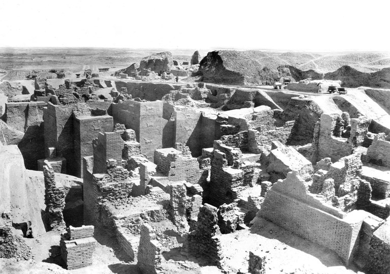 Black and white aerial photograph of the fragmentary brick wall remains of an archaeological site. Some portions of walls in the center of the photograph reveal vertical columns of raised relief brick dragons and bulls.