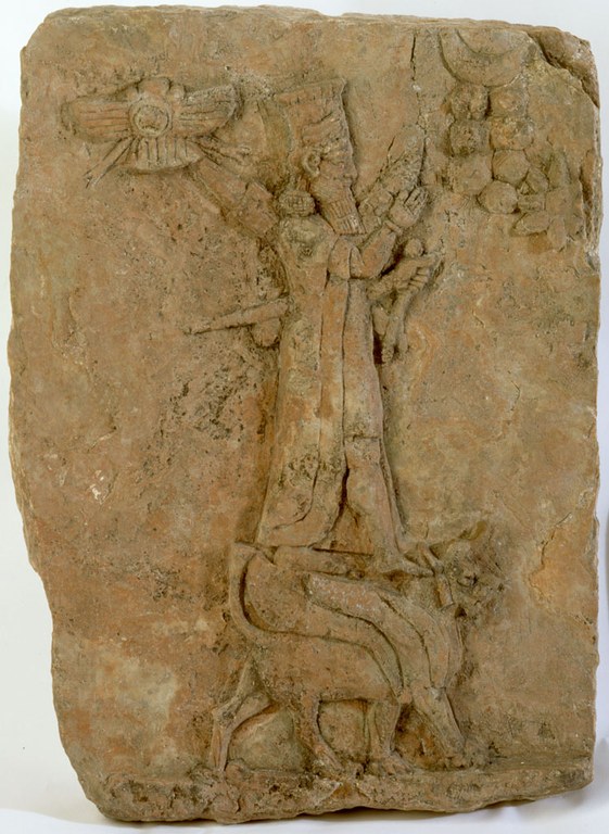 A clay tablet of a figure standing on a lion with divine symbols around him. The tablet is chipped around the edges and is grayish-brown in color.