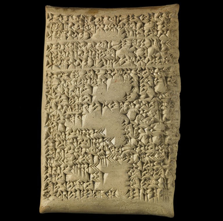 A rectangular brown clay tablet with many horizontal lines of cuneiform inscription. There are a few blank sections along the center. The tablet is photographed against a black background.