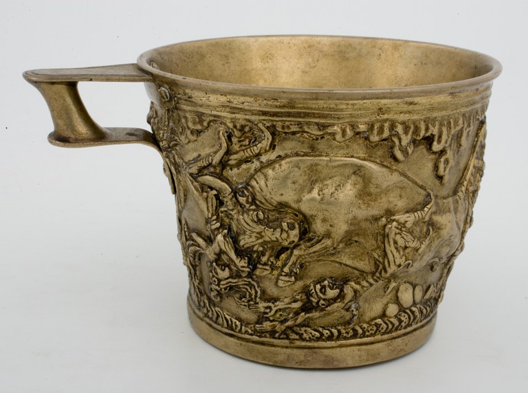 Photograph of a copper alloyed cup with a tiny handle and a raised relief design of a bull