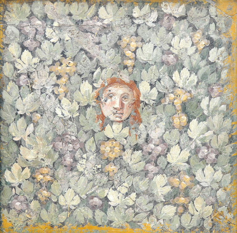 At the center a mask with eyes, nose, mouth, and red hair is surrounded by grape leaves and bunches of grapes. The mask’s eyes look directly out of the picture plane. The painting has a pastel color palette with pinks, greens, and oranges.