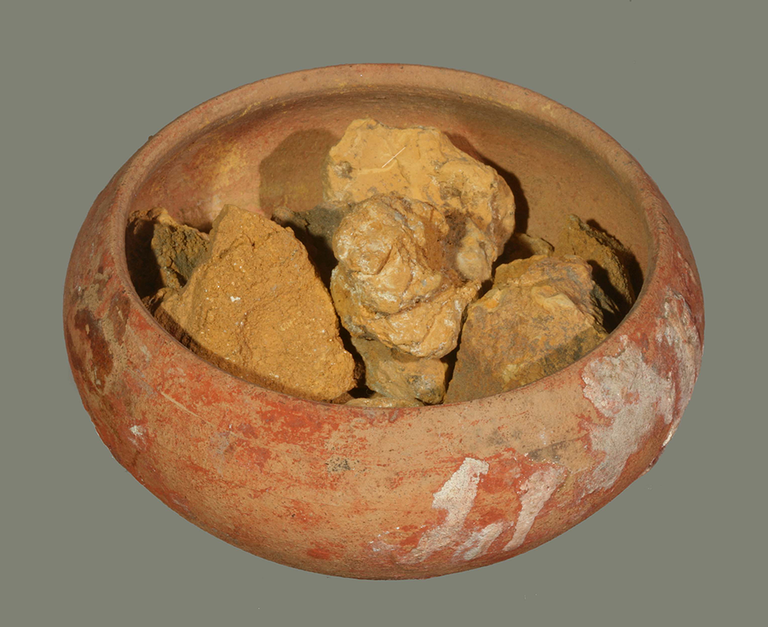 A terracotta cup with chunks of yellow pigment.