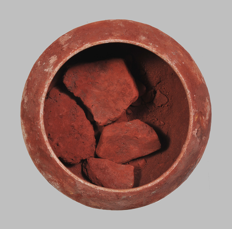 A terracotta cup with a large chunk of deep-red pigment.