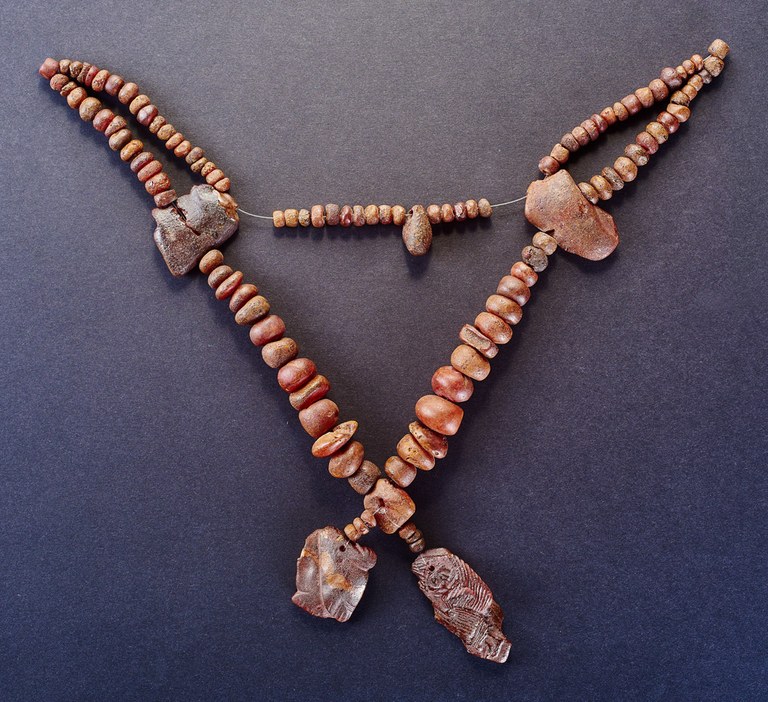 A long wire is strung with small round beads, three large irregularly shaped beads, and a long flat plaque with incised decoration.