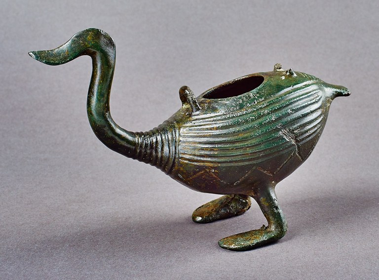 A vessel with a bird's stylized head, neck, legs, feet, and tail. The neck and body are incised with parallel lines.