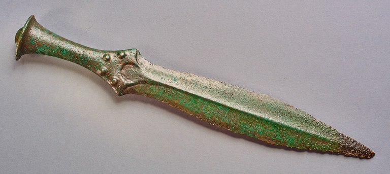 The undecorated blade has a rounded fuller, while the bottom of the grip is decorated with four large raised dots.