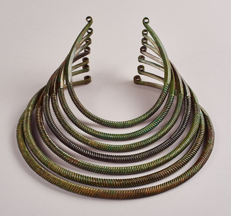 A metal collar composed of seven round, spirally grooved cylinders that decrease in size moving up to the next. Each cylinder extends to a rectangle that ends in a curve that forms a ring.