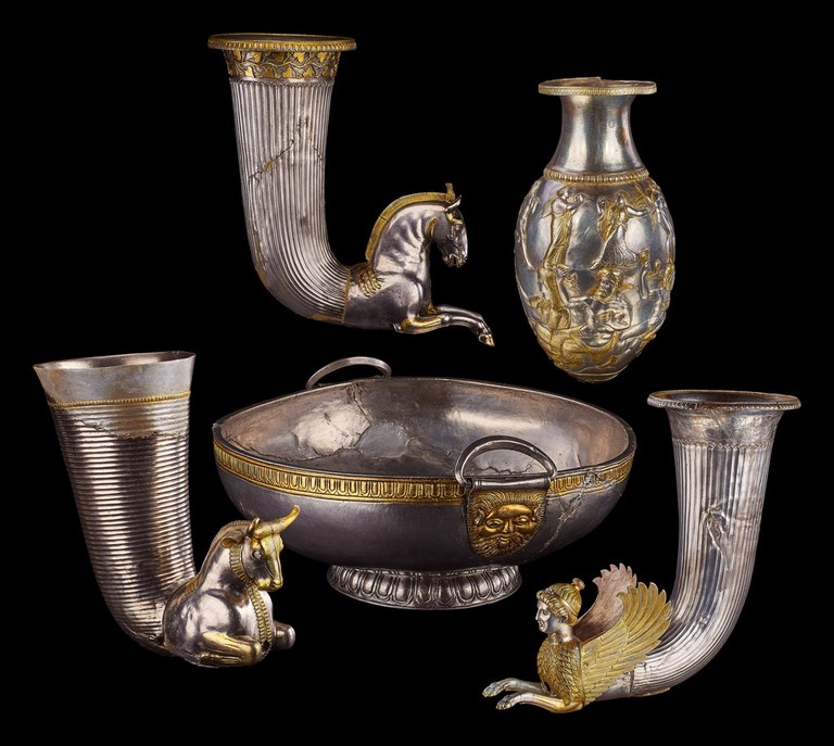 Three roughly conical vessels, one with a bottom ending in the head and neck of galloping horse, one in the head and neck of a bull, and one in the head and neck of a sphinx. A two-handled bowl decorated with a bearded human face. A vessel with a wide lip, narrow shoulder and rounded bottom, decorated with scenes of human figures.