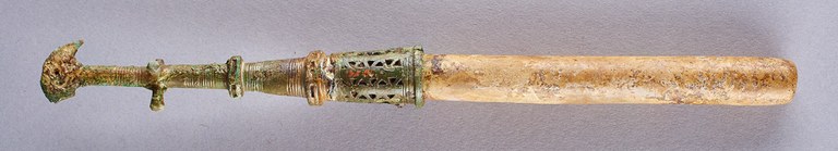 A long cylindrical stone with a metal handle. The shaft of the handle is decorated with incised and perforated linear and geometric designs.