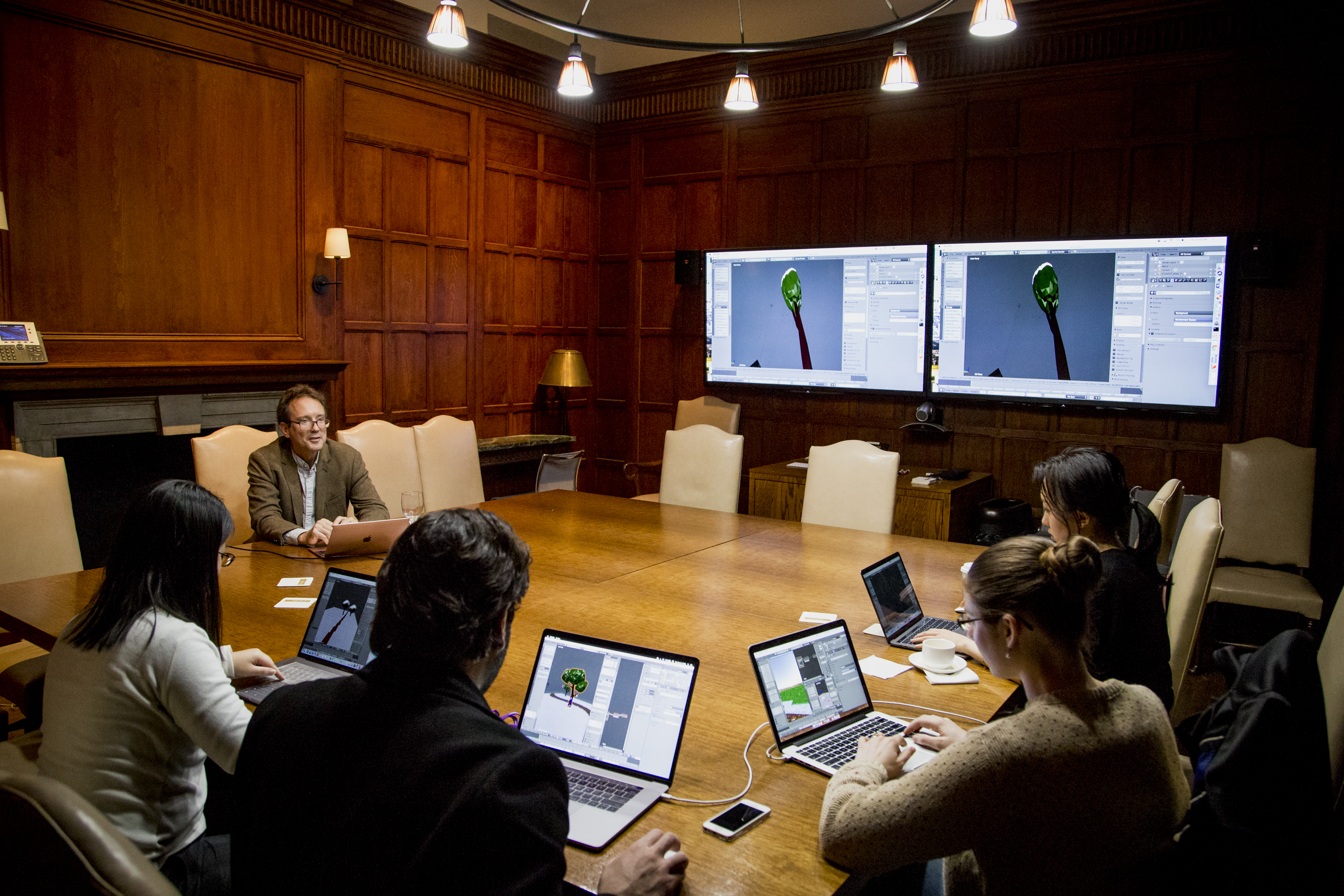 Professor and students with laptops around table in classroom