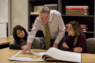 Group of three people look at map in folio book at table in library