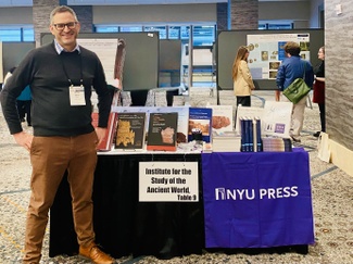 Associate Research Scholar Patrick J. Burns standing next to the ISAW Bookstall at the AIA/SCS 2026 book exhibition