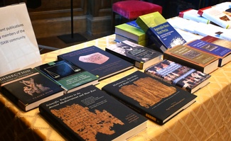 A series of books and articles published by the ISAW community displayed on a table